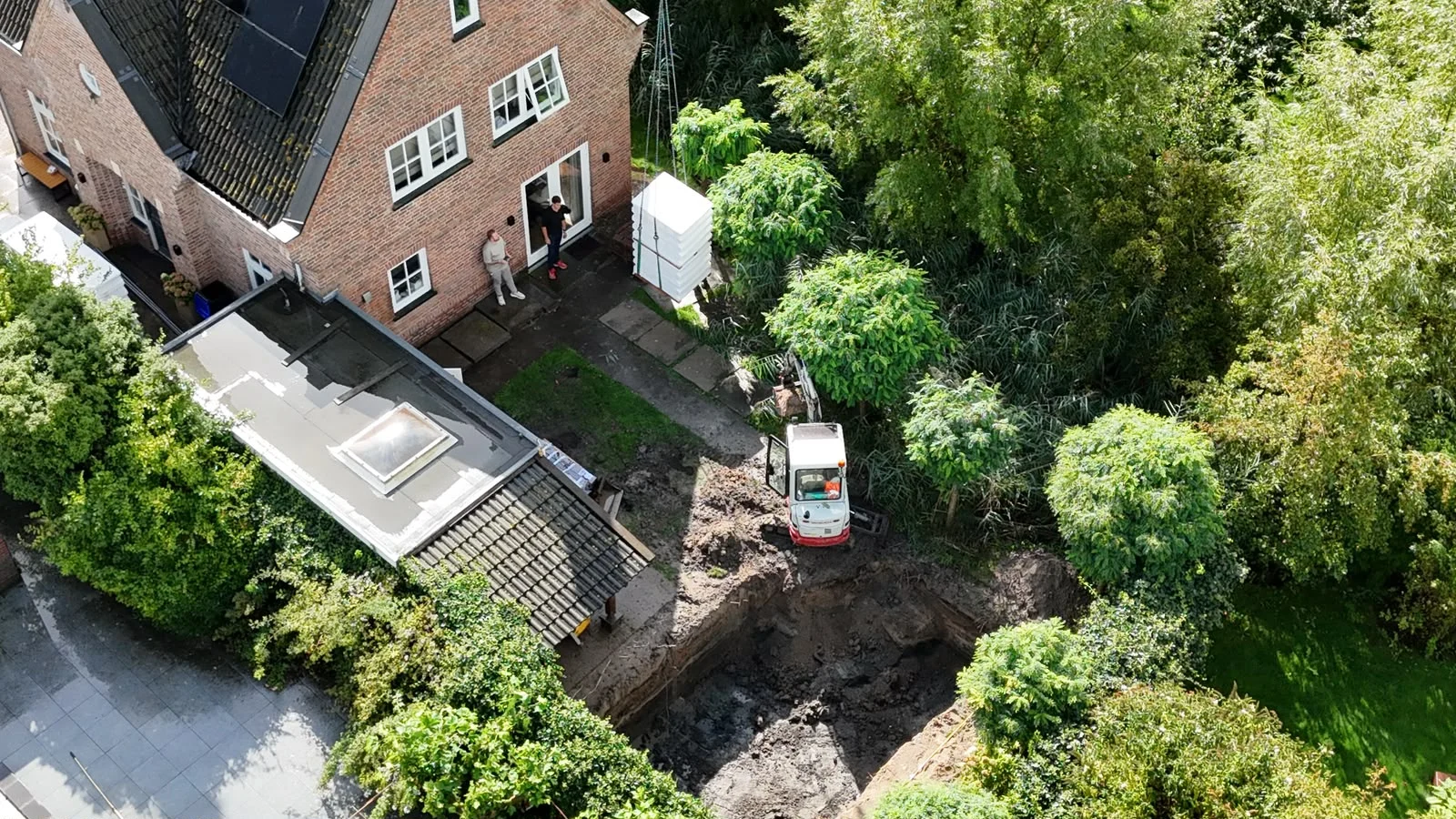 Midigraver bij een deels ontgraven bouwput in een achtertuin